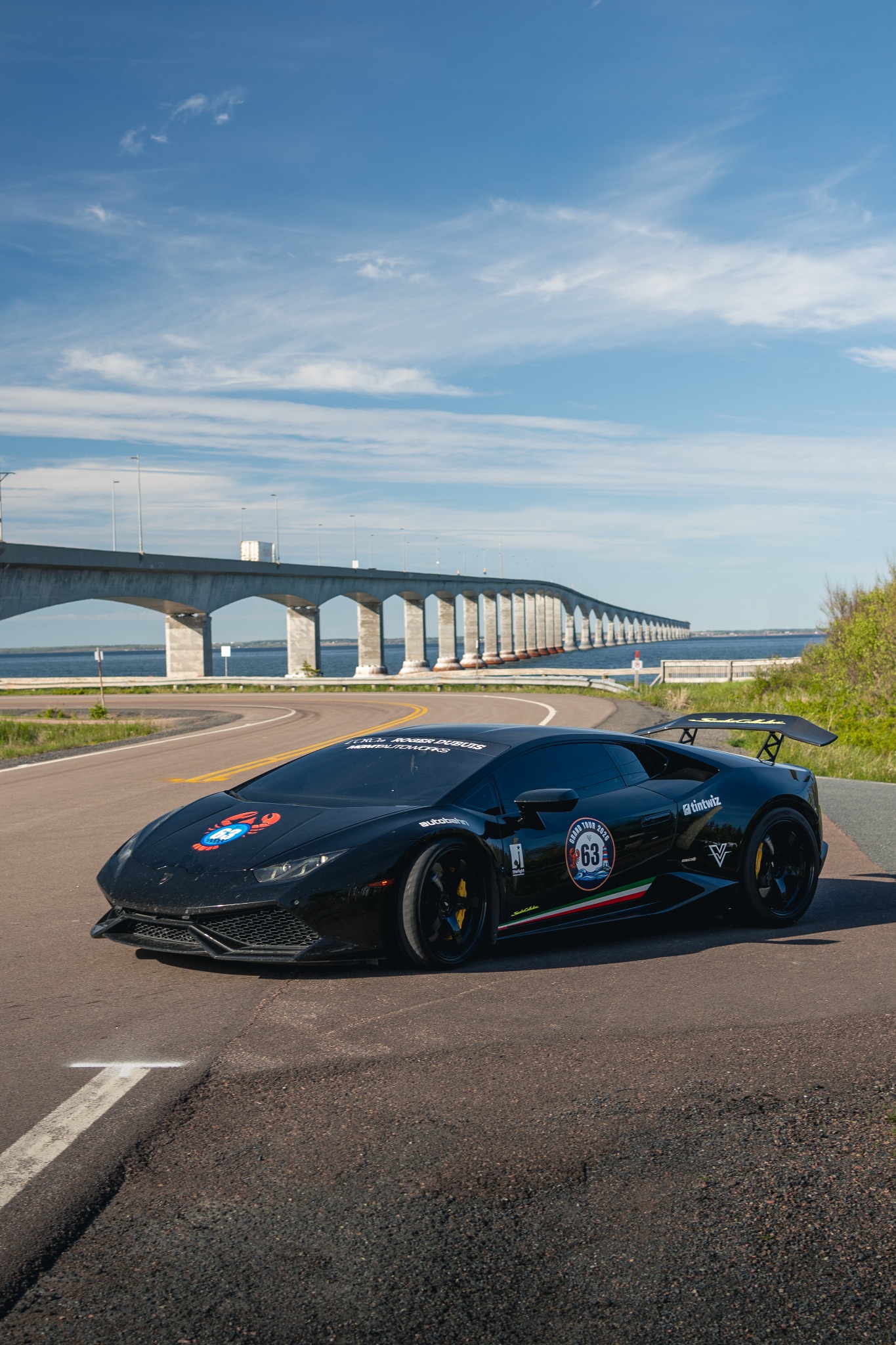 The original black Huracán beside a waterfront bridge.